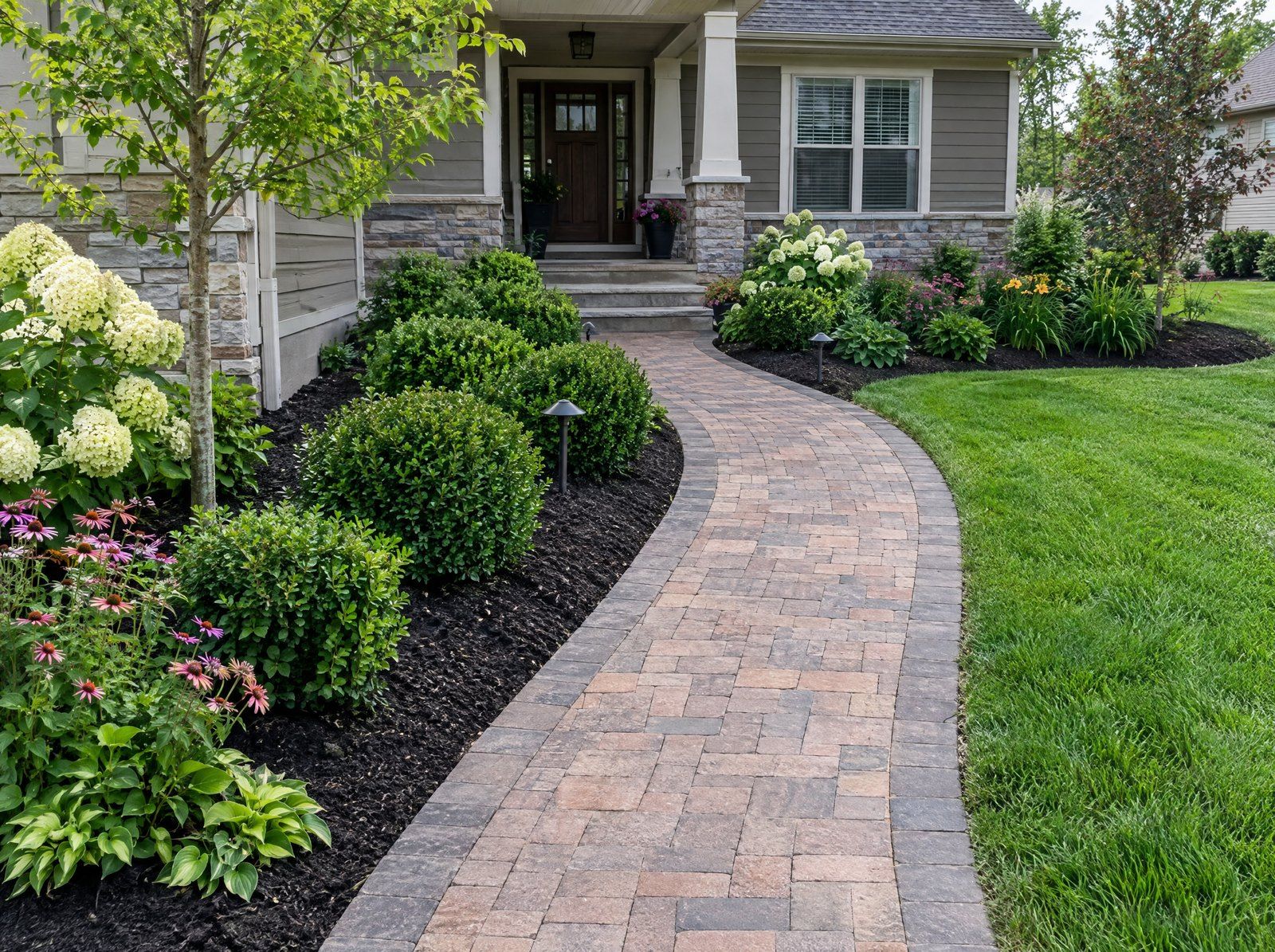 Curved brick paver walkway leading to a front porch through fresh planting beds