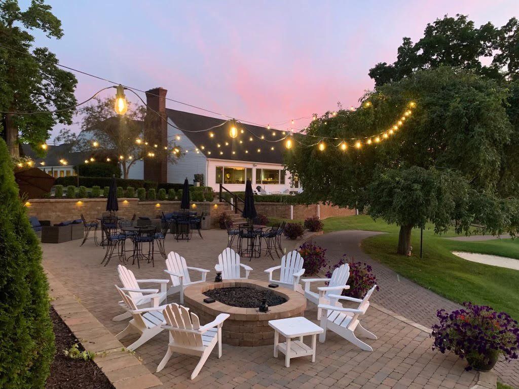 Paver patio with a fire pit and seating at dusk under string lights