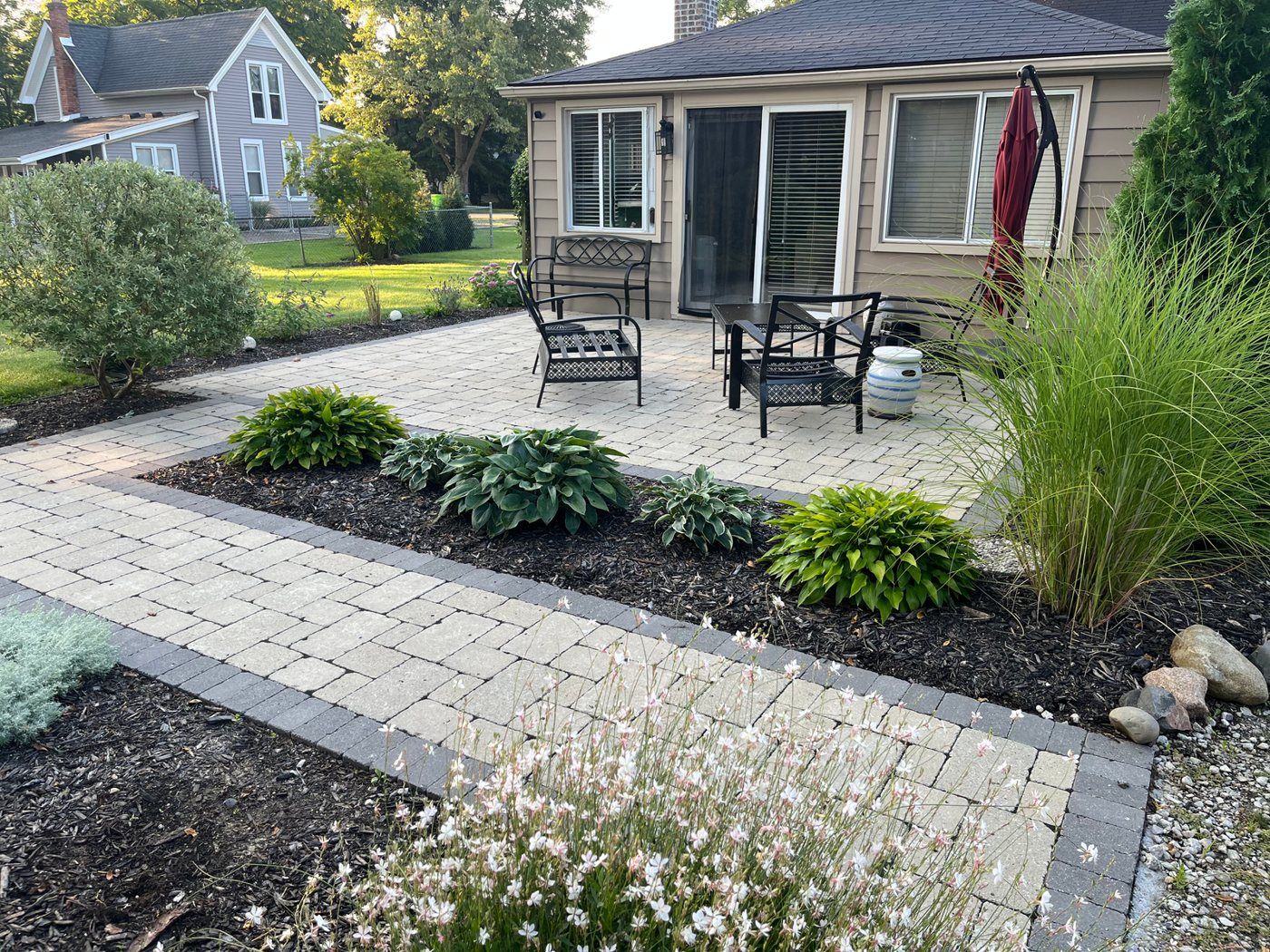 Finished brick paver patio with planting beds behind a home